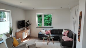 A modern living room with a sofa, a coffee table, a TV, and a window with a view of greenery.