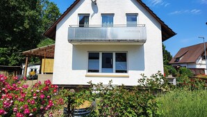 A two-story house with a balcony, a satellite dish, and a garden with flowers.