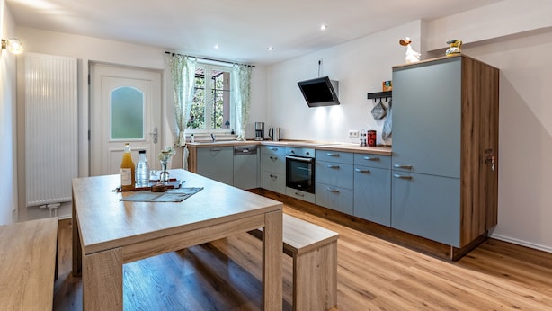 A modern kitchen with a wooden table, a built-in oven, and a TV mounted above the cabinets.
