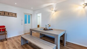 A dining area with a wooden table and bench, a red chair, and a wall-mounted light fixture.