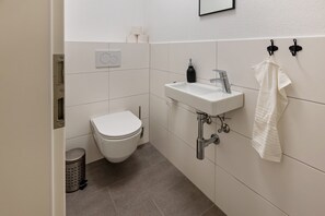 Un baño pequeño y moderno con inodoro, lavamanos y toallero.