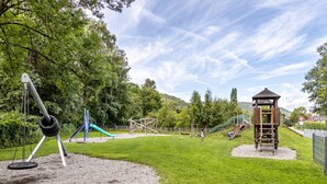 A playground with swings, slides, and climbing structures surrounded by trees and a grassy area.