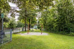 Un parque infantil con columpios y una zona vallada, rodeado de árboles.