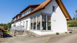 Une maison à deux étages, dotée d’un toit en pente, de grandes fenêtres et de fondations en pierre.