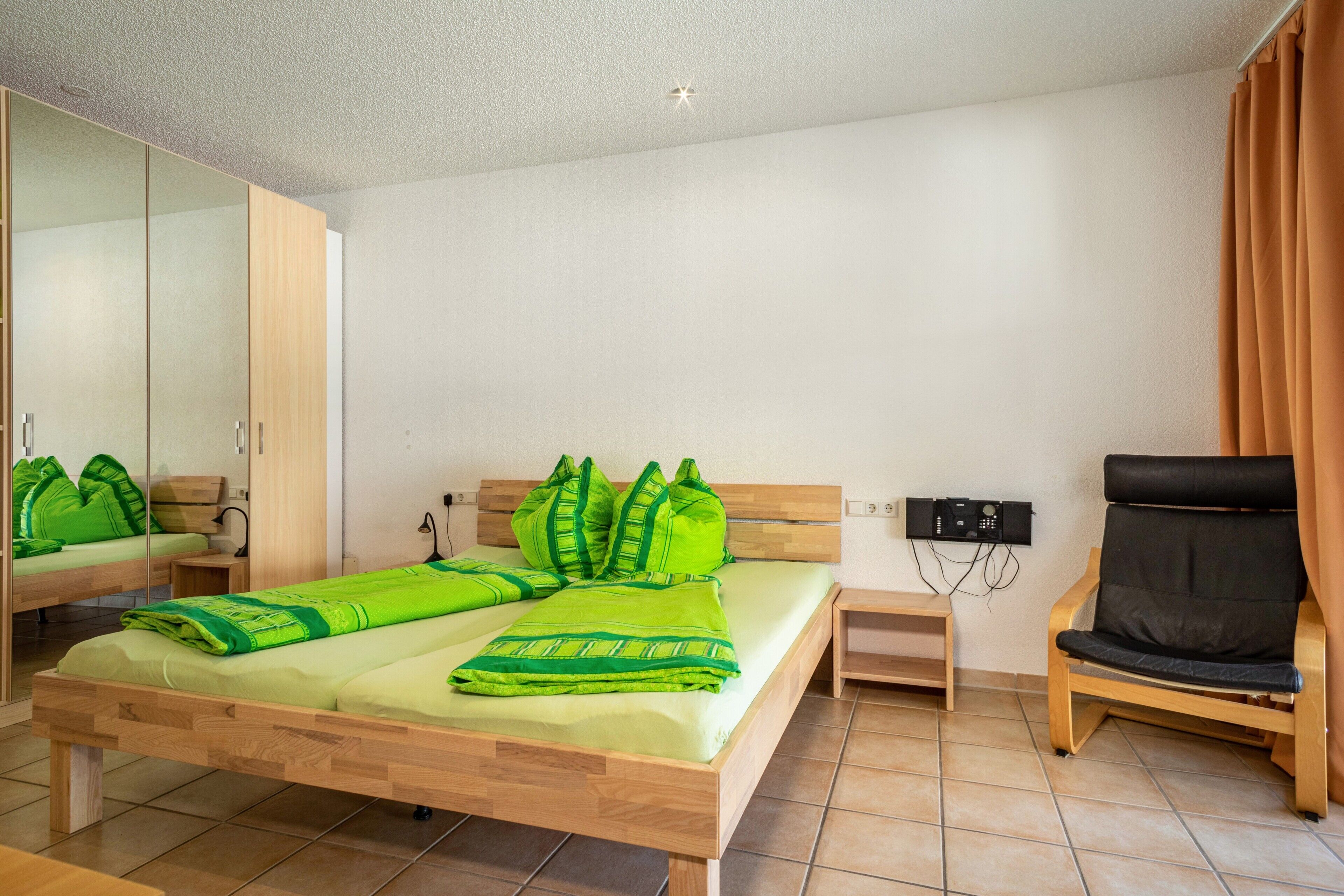Una habitación con cama, una silla, un escritorio, un espejo y un dispositivo en la pared.