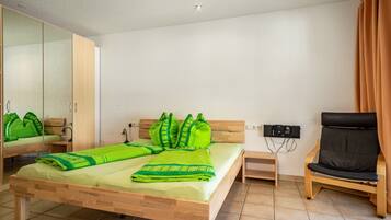 Una habitación con cama, una silla, un escritorio, un espejo y un dispositivo en la pared.