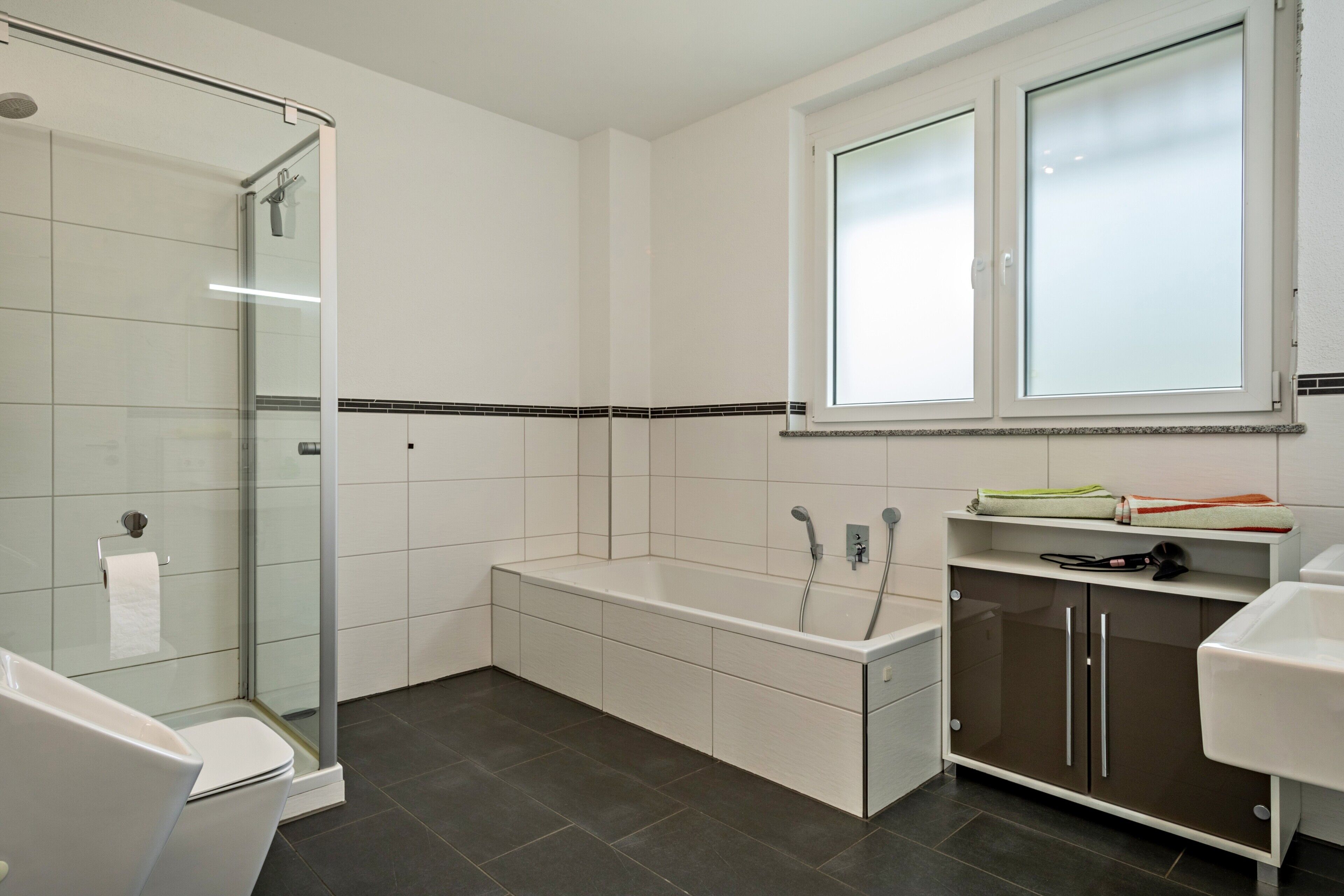 Een moderne badkamer met een douchecabine van glas, een badkuip en een wastafel met spiegel.