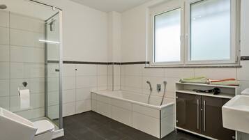 Een moderne badkamer met een douchecabine van glas, een badkuip en een wastafel met spiegel.