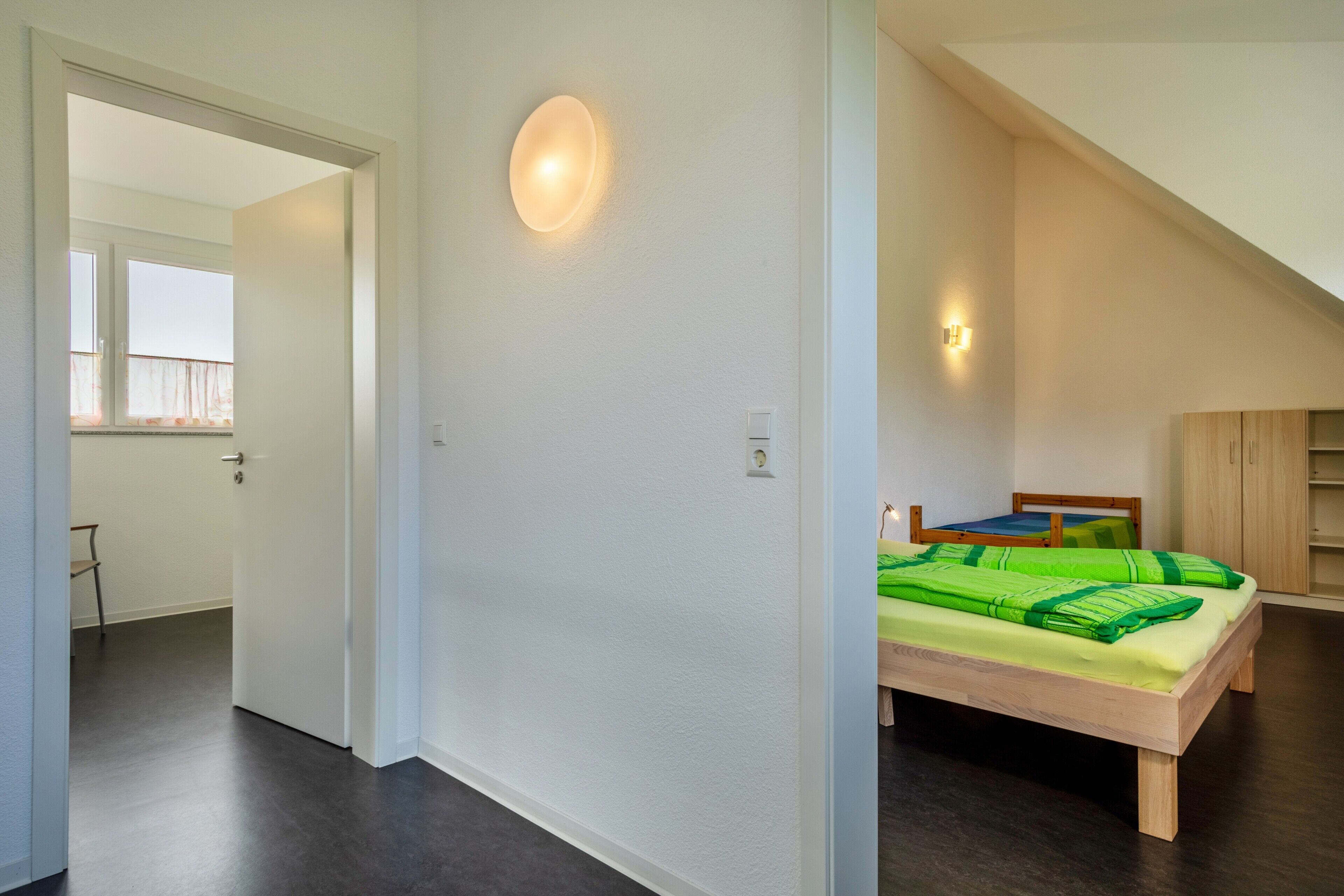 Ein Schlafzimmer mit Bett, Fenster und einer Tür zu einem anderen Raum.
