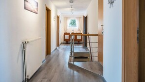 Un pasillo con radiador, suelo de madera, ventana con cortinas y una puerta a la derecha.