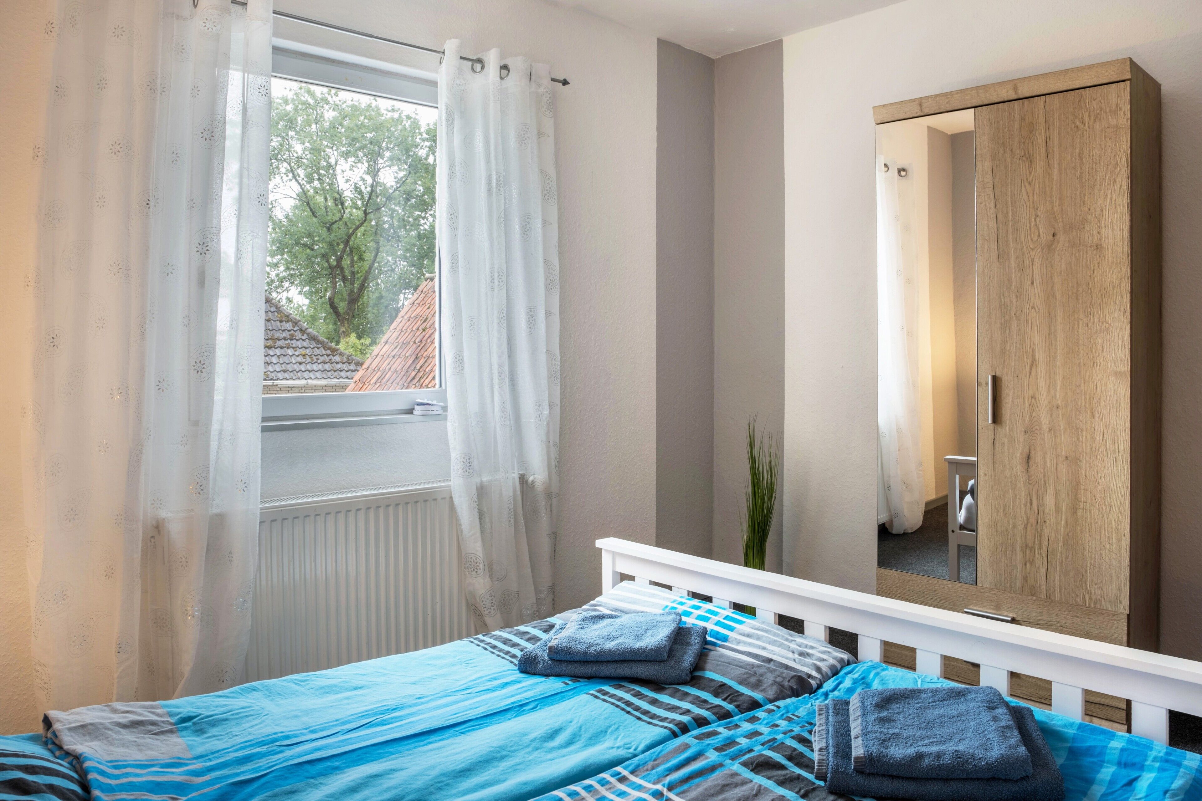 Une chambre à coucher avec un lit, une fenêtre avec des rideaux, un miroir et un radiateur.