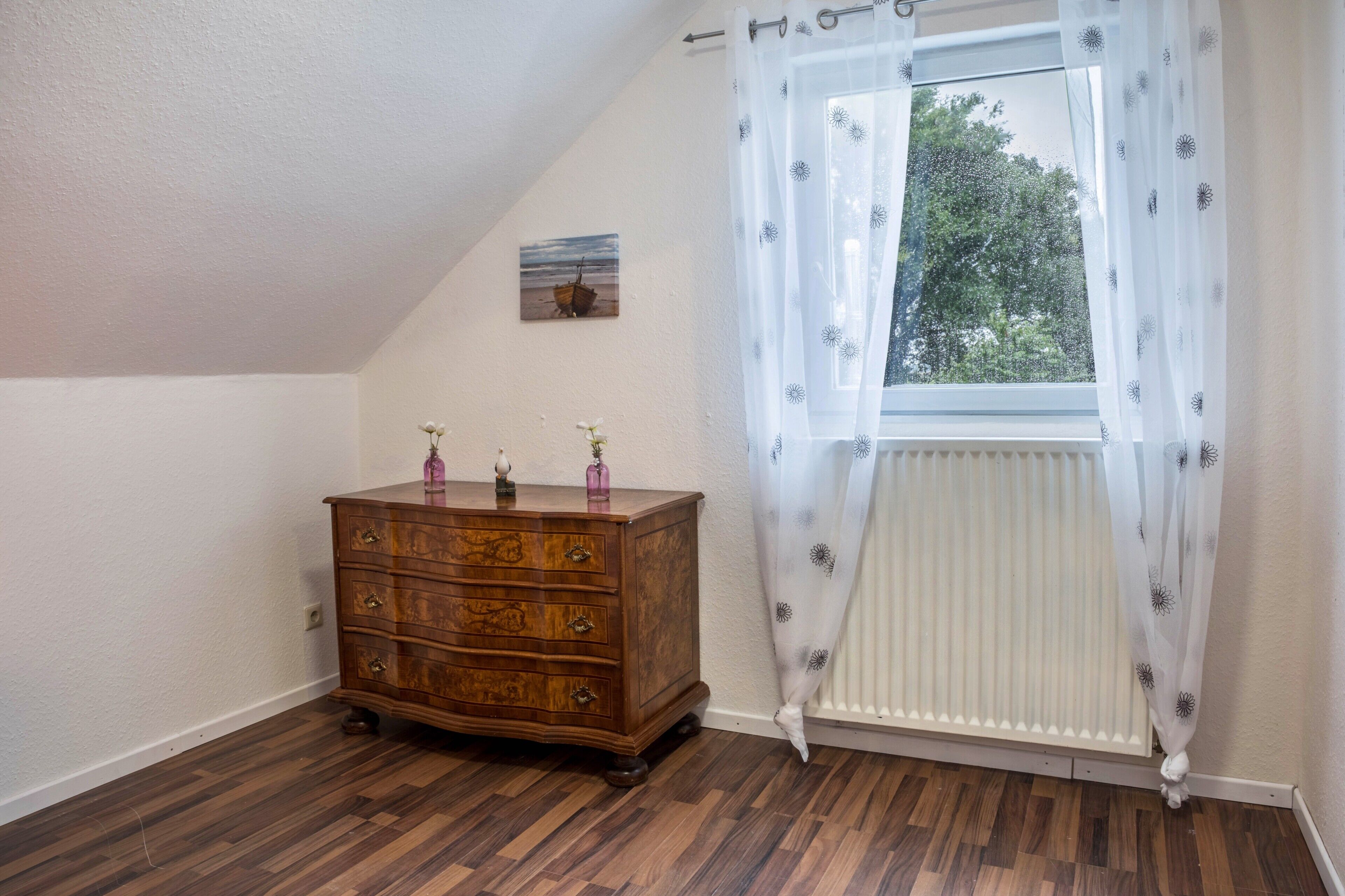 Una habitación con un aparador de madera, un radiador y una ventana con cortina.