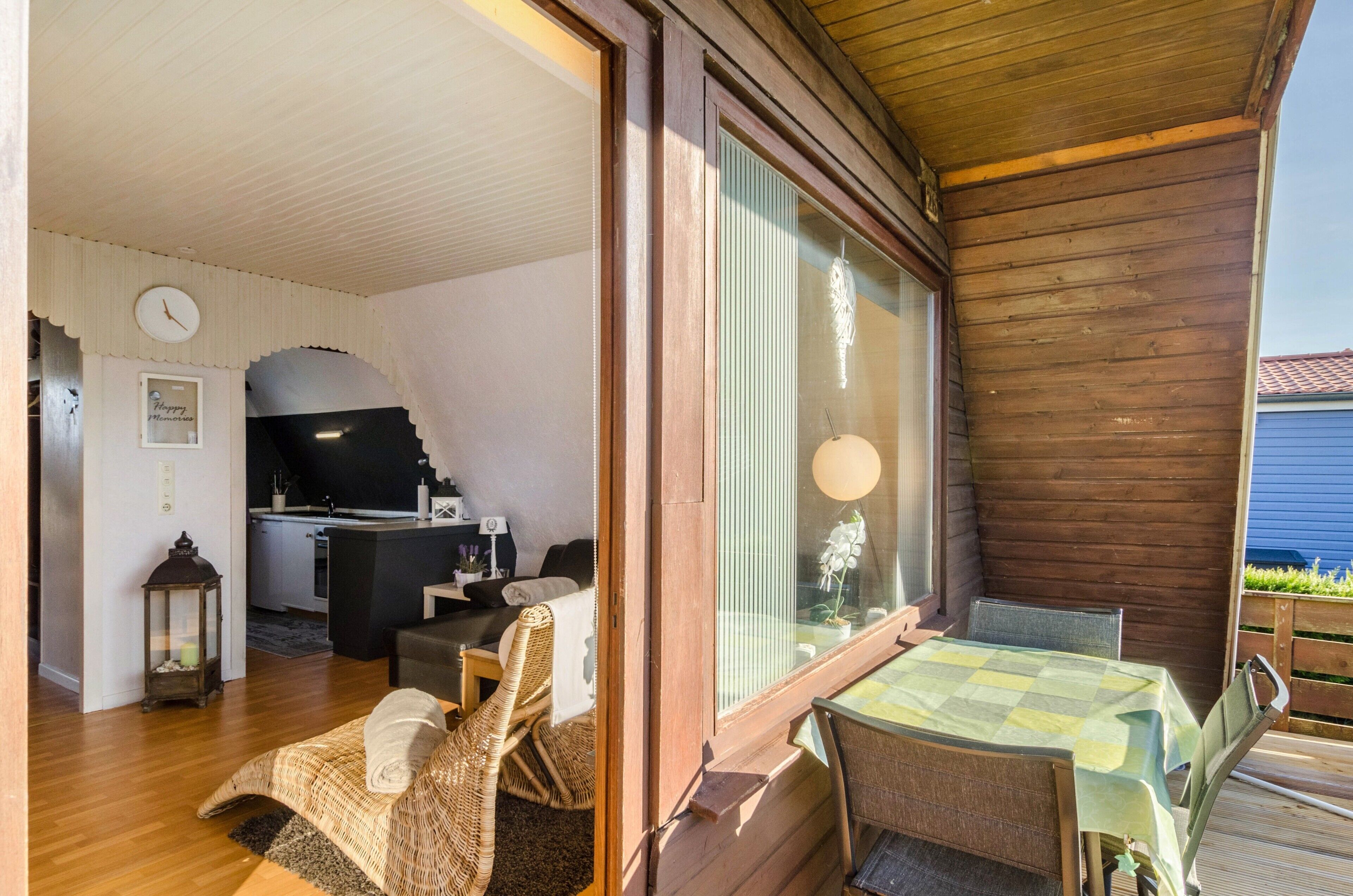 A cozy room with a dining table, wicker chairs, a small kitchen area, and a large window.
