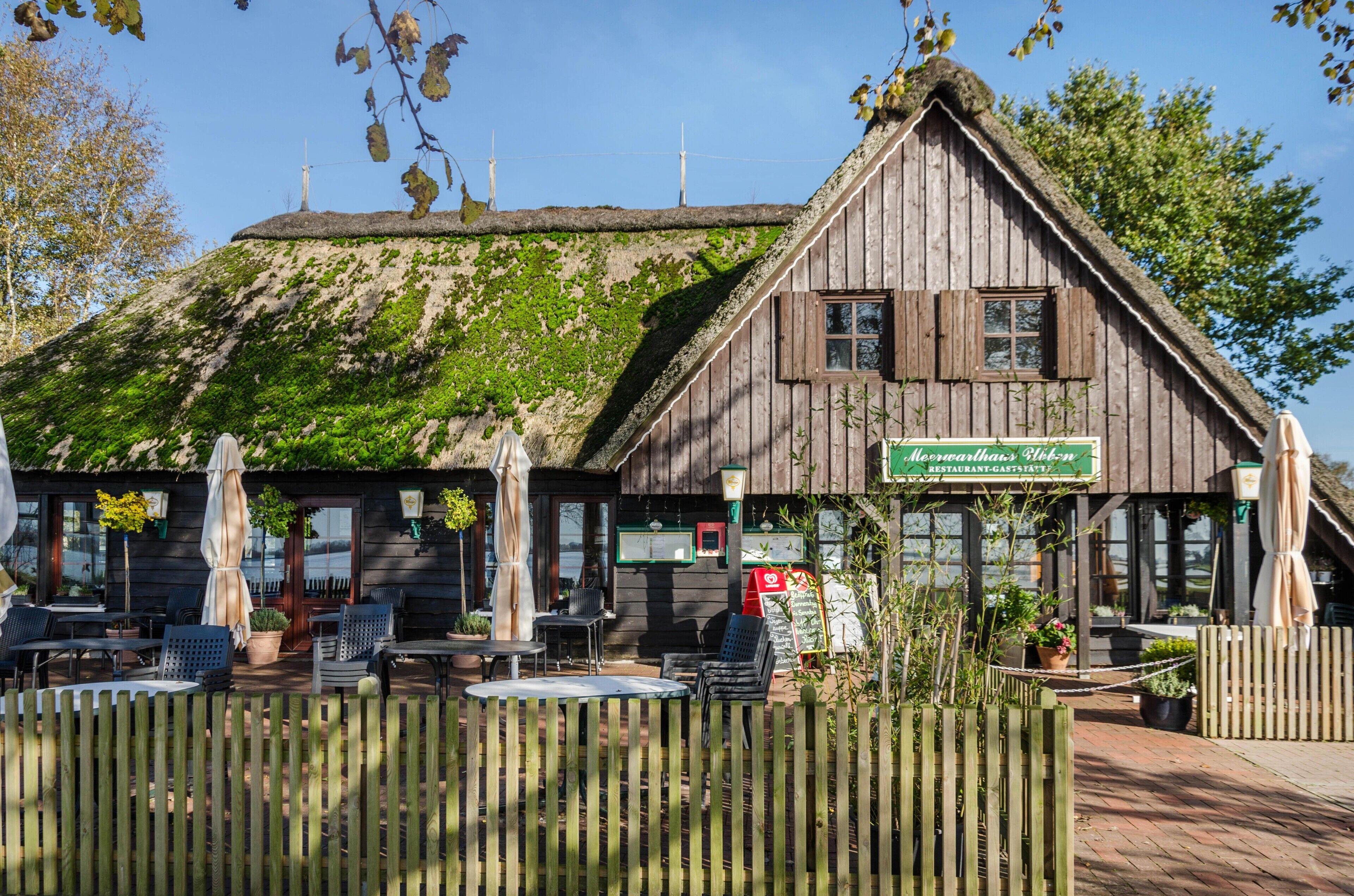 A wooden building with a thatched roof, outdoor seating, and a sign indicating a restaurant.