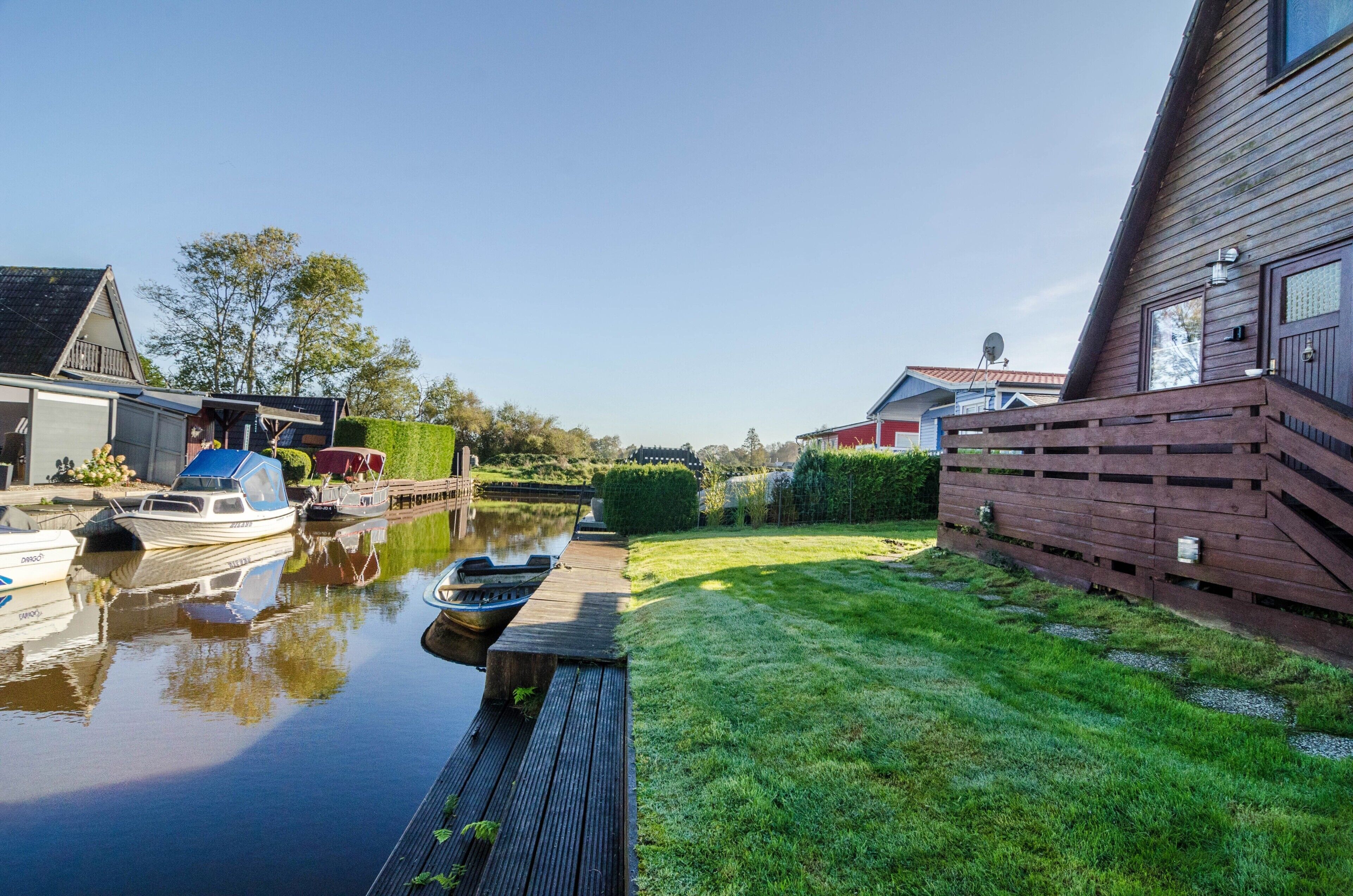 Une propriété située au bord d’un canal, dotée d’un quai en bois, d’un bateau et d’une pelouse bien entretenue.