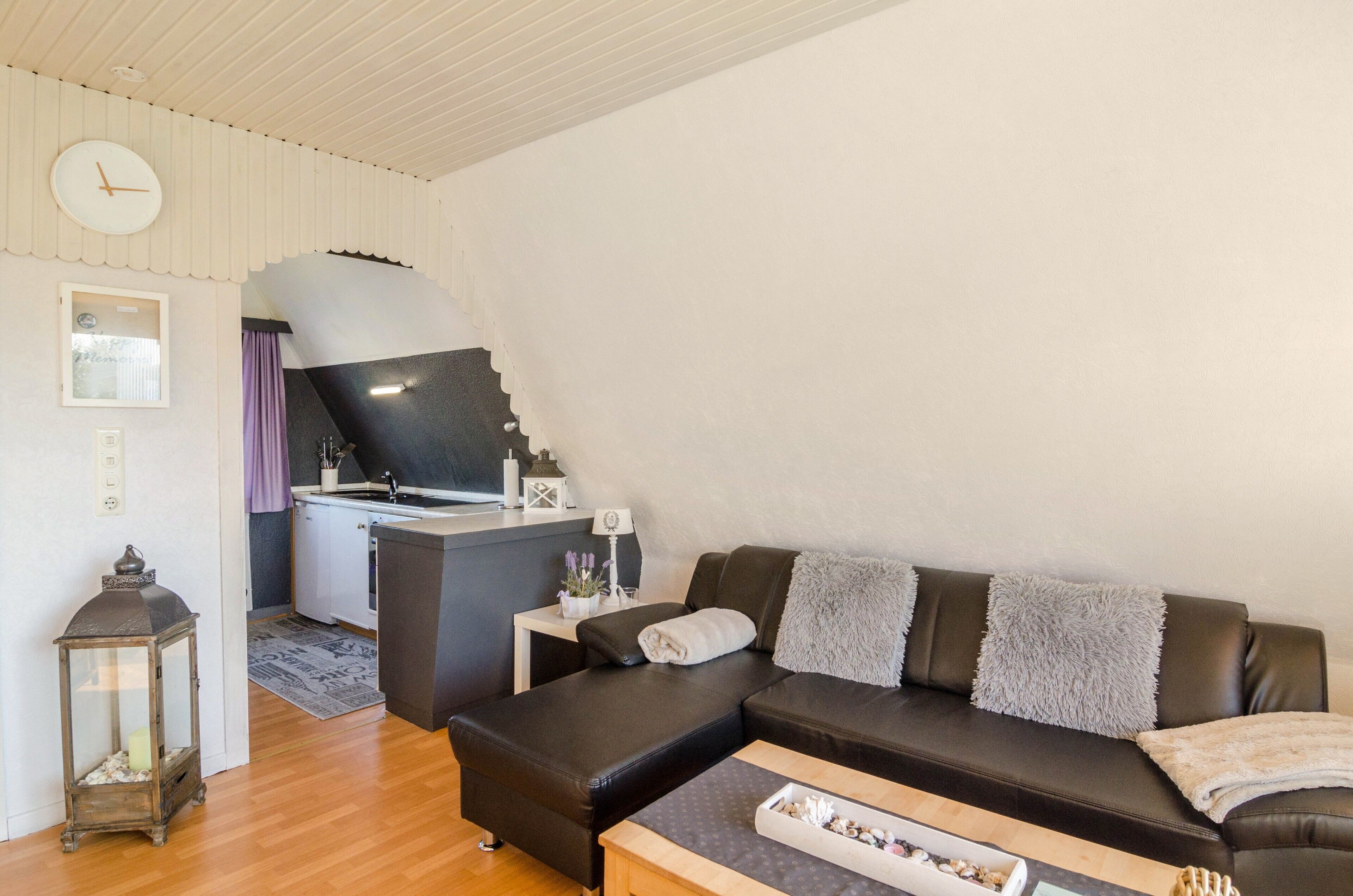 A modern living room with a sofa, a small table, a lamp, and a kitchen area with a sink and cabinets.