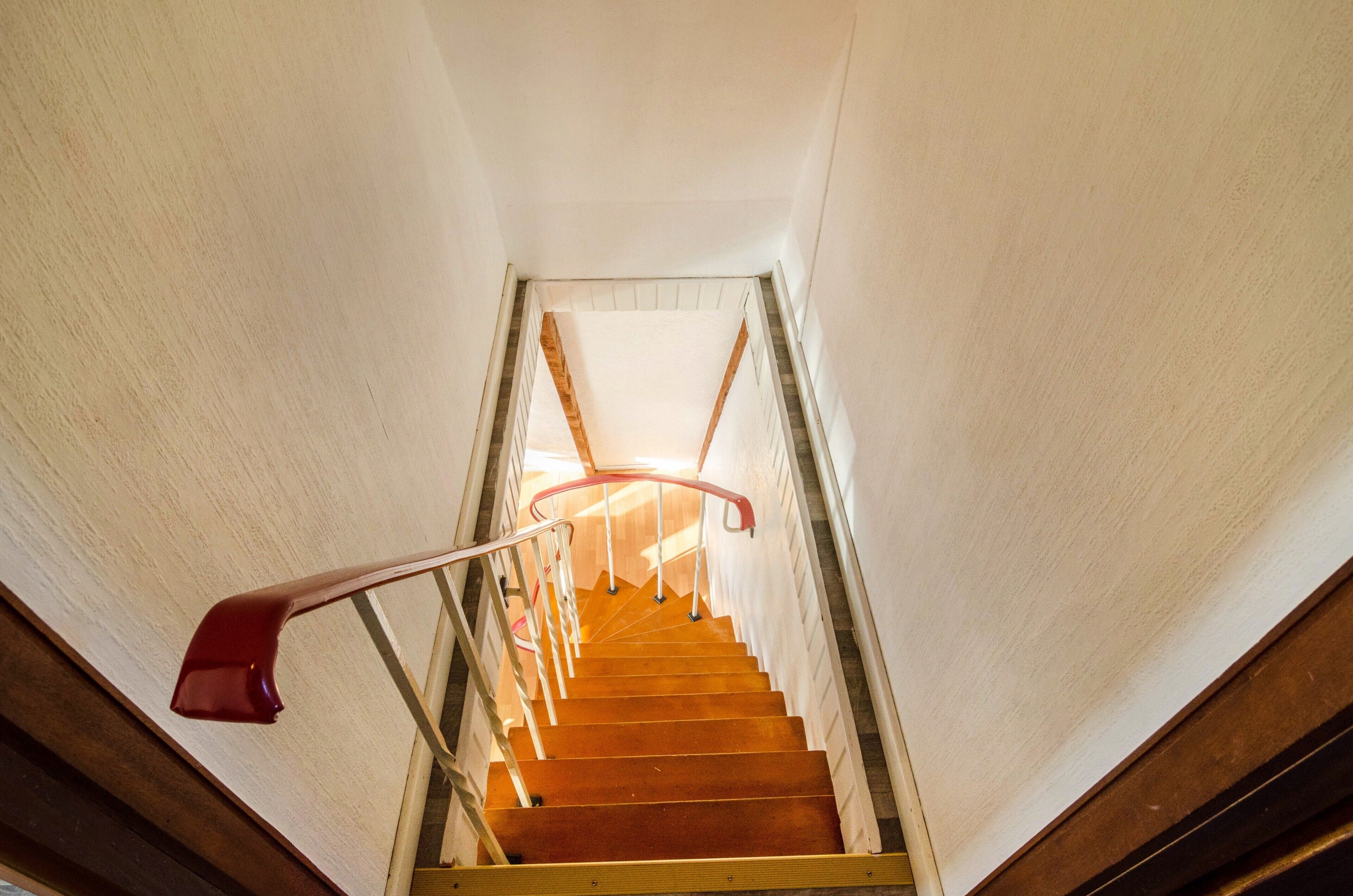 Eine Holztreppe mit Handlauf und einem roten Gegenstand links.