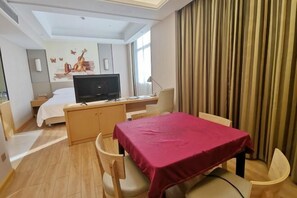 Una habitación de hotel con cama, escritorio con computadora, televisión y un área de comedor con mesa y sillas.