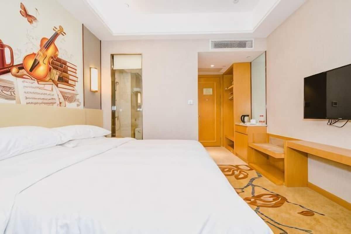 Una habitación de hotel con una cama grande, televisión, escritorio y espejo.
