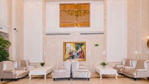 Een ruime lobby met een hoge plafond, een groot schilderij en zitgelegenheid.