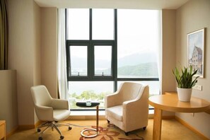 Una habitación con un ventanal grande, dos sillas, una mesita y una planta en maceta.
