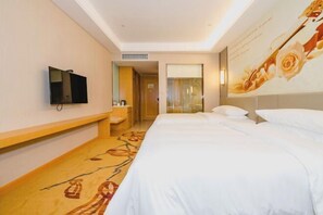 Una habitación de hotel con cama, televisor montado en la pared, un pequeño rincón de descanso y un detalle decorativo en la pared.