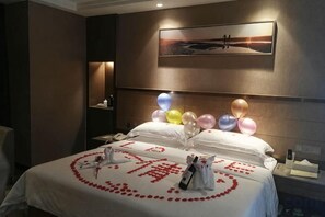 A hotel room with a bed adorned with a heart-shaped arrangement of rose petals and a bouquet of flowers. - Weina International Hotel (Qiandao Lake) (Chun'an)