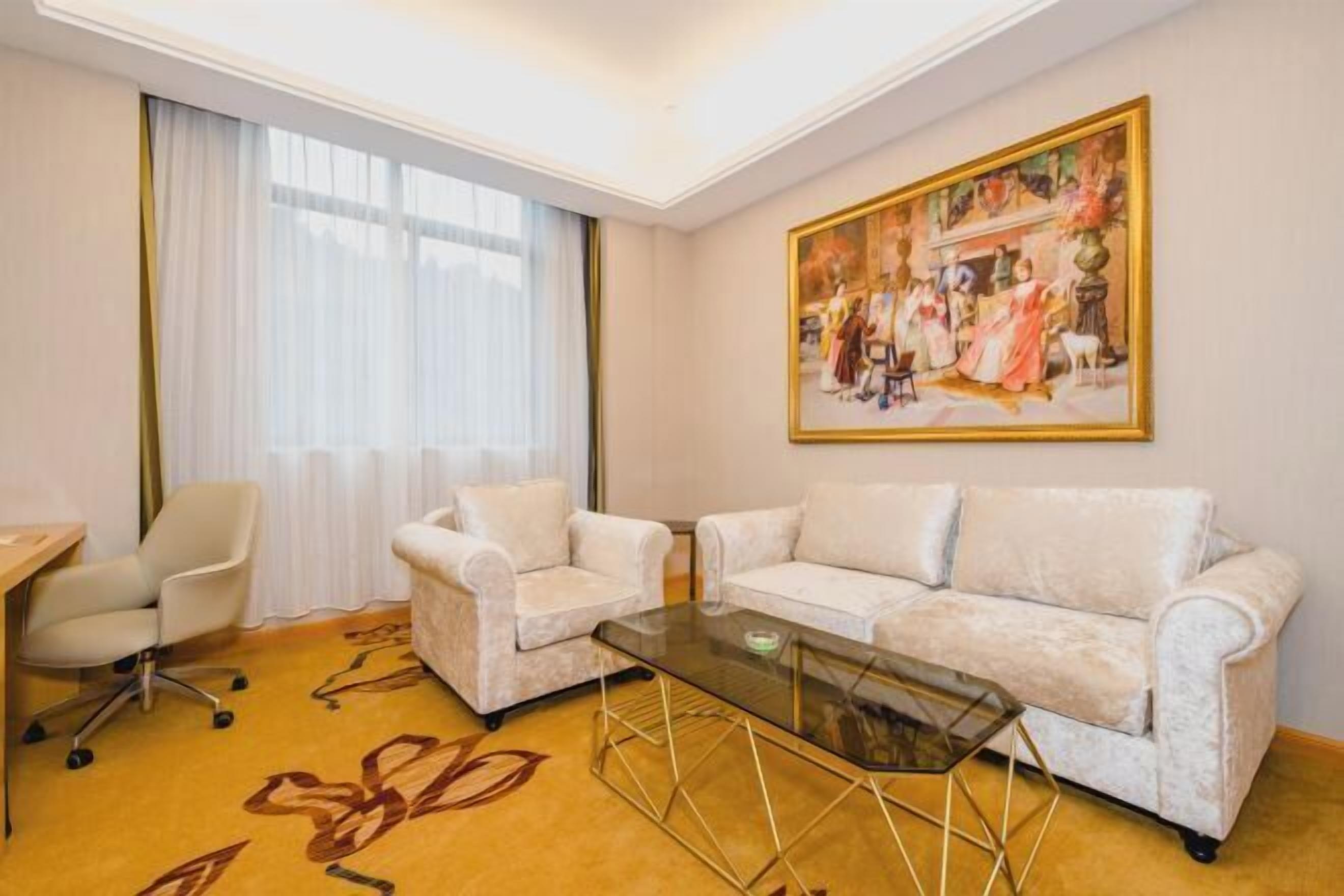 Une pièce comprenant un canapé, une table basse en verre, un bureau et un tableau accroché au mur.