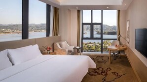 Een hotelkamer met een groot bed, een bureau, een stoel, een televisie en uitzicht op een meer en bergen.