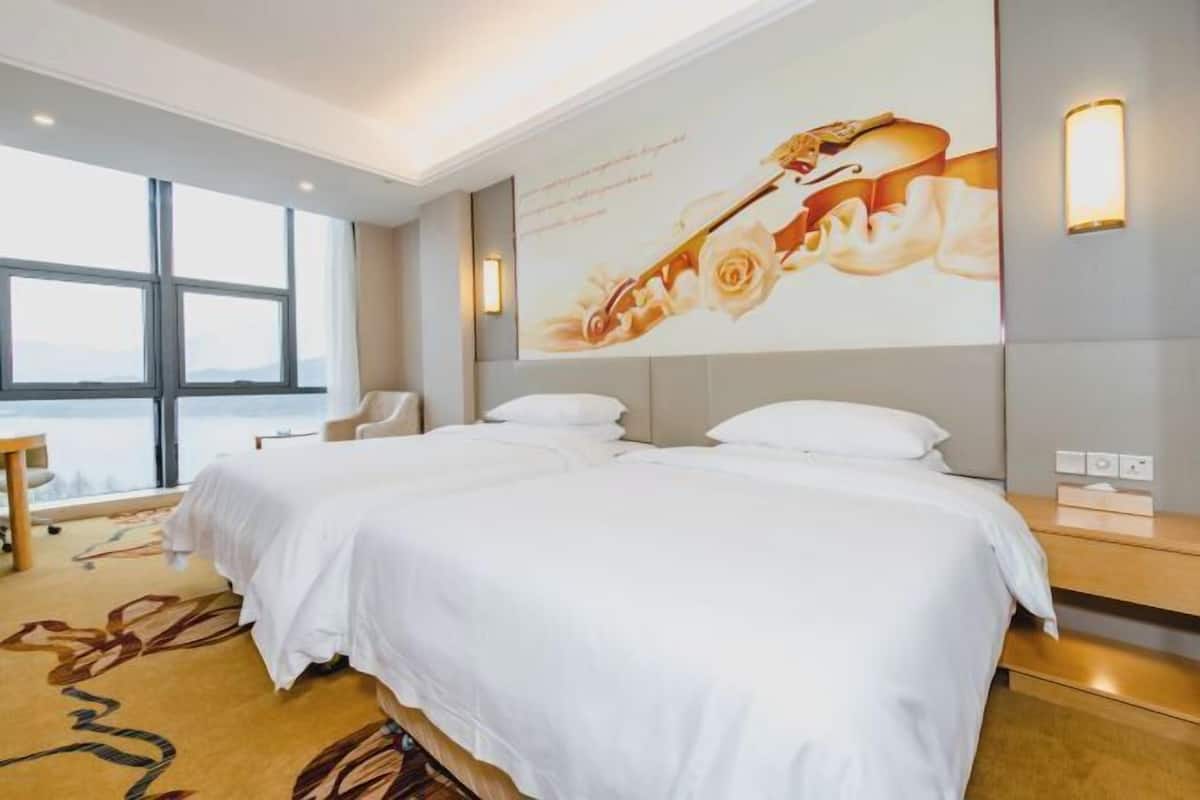 Una habitación de hotel con dos camas, un ventanal amplio, una obra de arte en la pared y una mesita de noche.