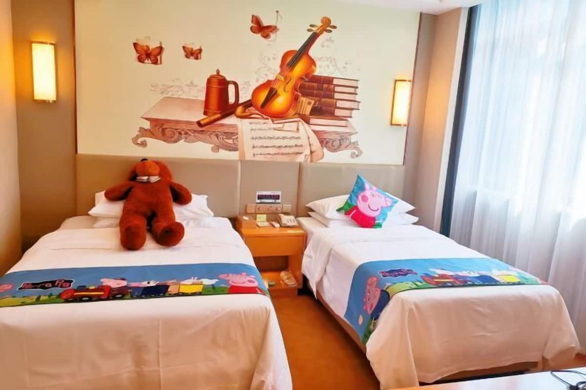 Habitación de hotel con dos camas, un mural en la pared, un oso de peluche y una mesita de noche con un teléfono.
