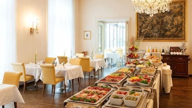 Een eetruimte met meerdere tafels, een buffet met diverse gerechten en een kroonluchter.