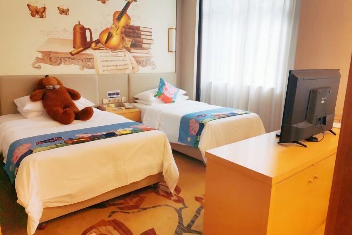 Habitación de hotel con dos camas, un televisor sobre un aparador de madera, y una pared decorada con una guitarra y libros.