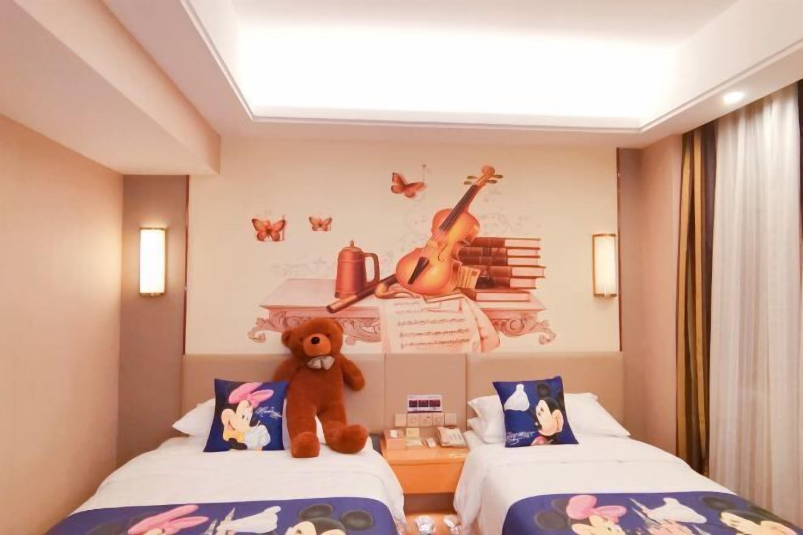 A hotel room with two beds, a teddy bear, a violin, and a wall mural.