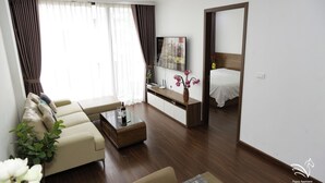A modern hotel room with a sofa, a coffee table, a TV, and a bed. - Pegasy Apartments & Travel (Hanoi)
