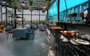Un ristorante con terrazza sul tetto, tavoli, sedie, angolo bar e vista sulla città.