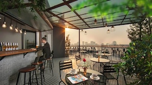 A rooftop bar with a bartender, tables, chairs, and a city skyline view. - Pegasy Apartments & Travel (Hanoi)
