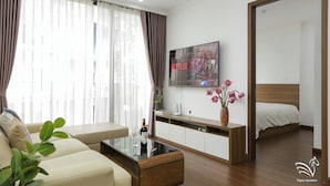 A modern hotel room with a sofa, a coffee table, a TV, a bed, and a mirror. - Pegasy Apartments & Travel (Hanoi)