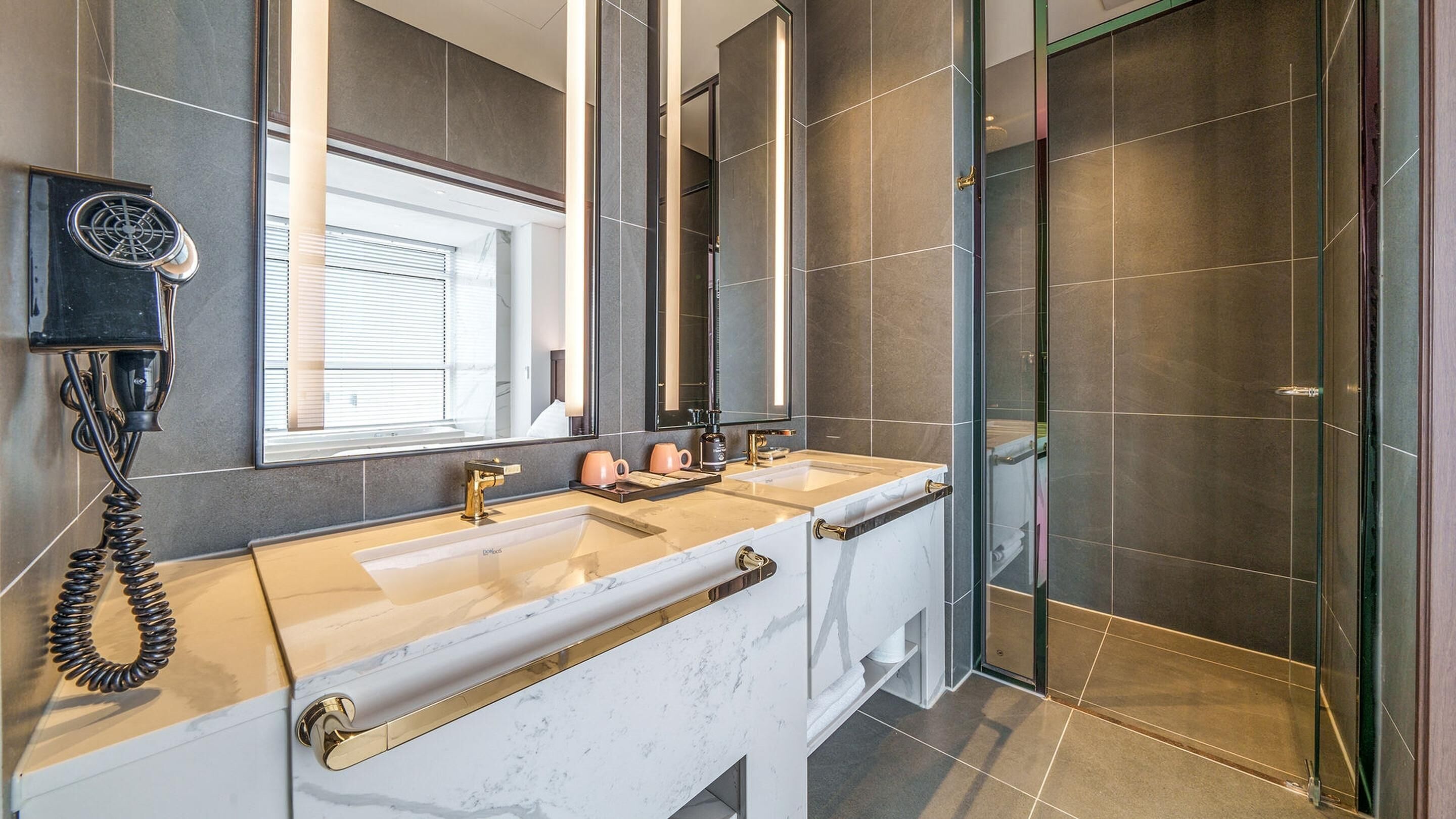 Ein modernes Badezimmer mit zwei Waschbecken, einem großen Spiegel und einer begehbaren Dusche.