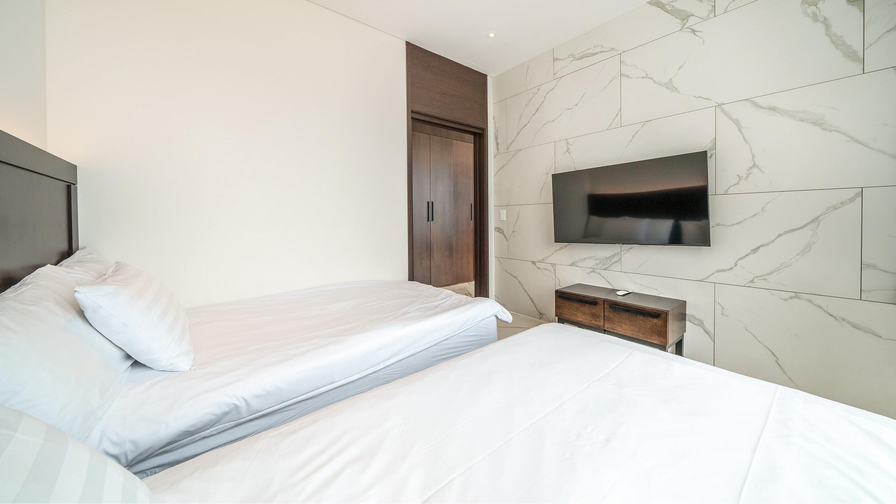 Una habitación de hotel moderna con una cama, un televisor montado en la pared y un armario de madera.