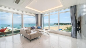 A spacious living room with a large window offering a view of the beach and ocean. - Goseong Moneblue Pension (Goseong)