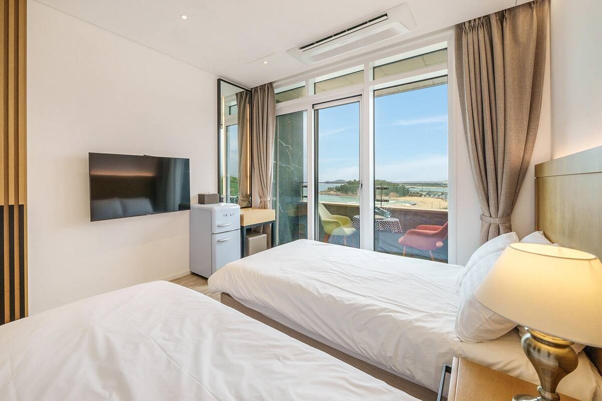 Habitación de hotel con dos camas, televisión, escritorio y vista a la playa.