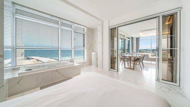 A modern bedroom with a large bed, a bathroom with a bathtub, and a dining area with a view of the ocean. - Goseong Moneblue Pension (Goseong)
