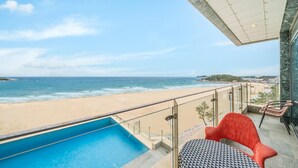 A balcony with a pool, a red chair, and a view of the beach and ocean. - Goseong Moneblue Pension (Goseong)