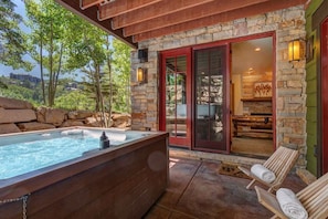 A hot tub with wooden seating, stone walls, and a glass door leading to an interior space.