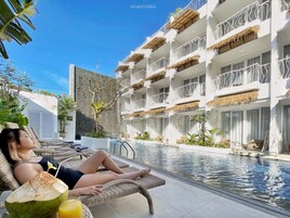 Una mujer descansando junto a una piscina en una tumbona, con una bebida y un coco.