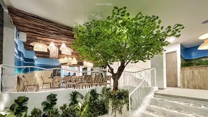 Eine Treppe mit Baum und Pflanzen, ein Sitzbereich mit Korbmöbeln und eine Wand mit einem blauen Wandgemälde.