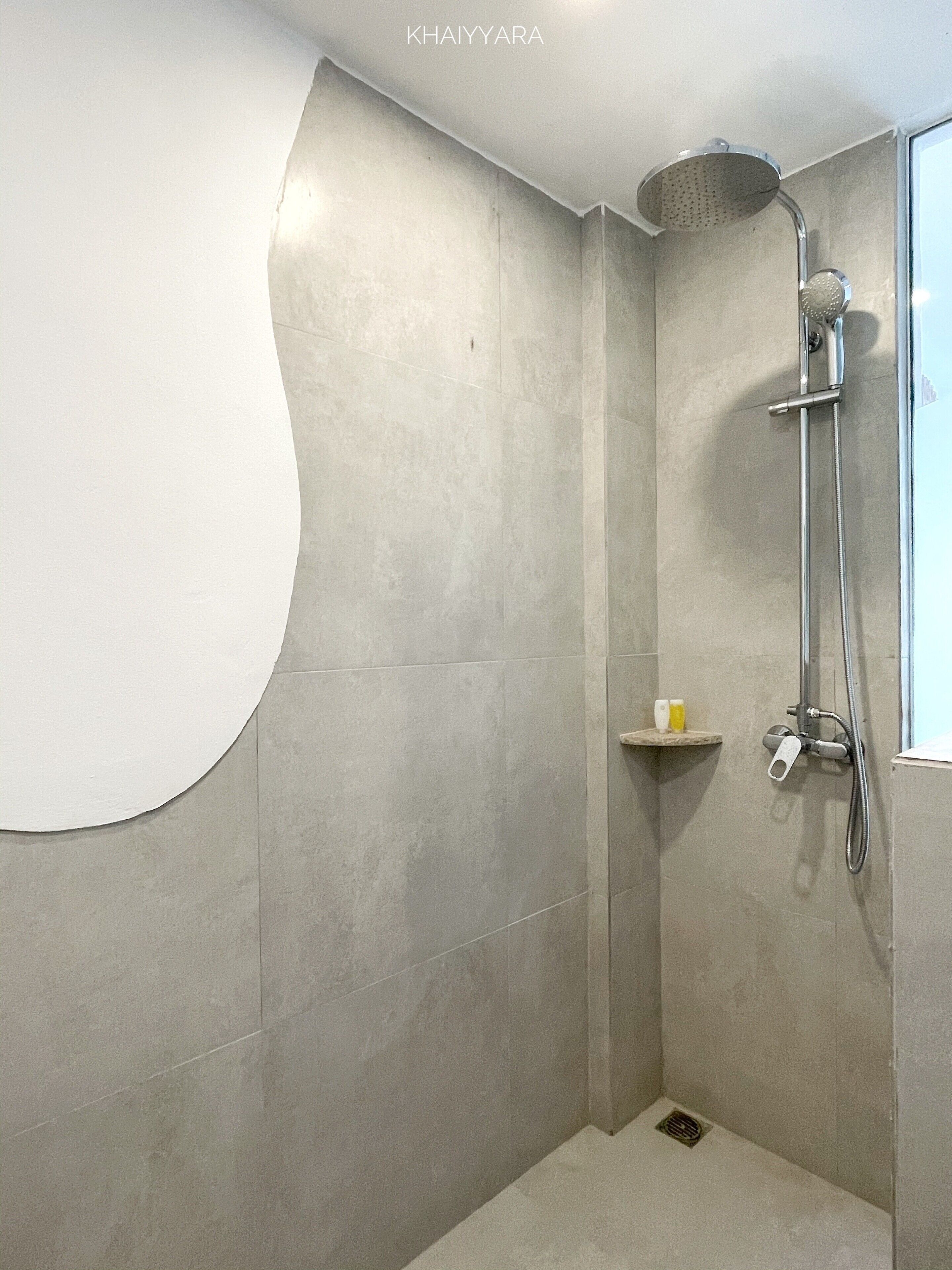 A modern shower with a curved wall design, a handheld showerhead, and a small shelf with toiletries.