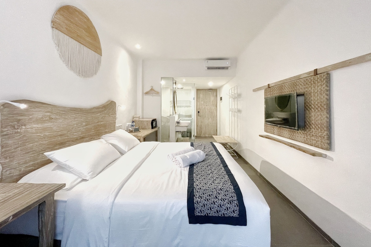 Een hotelkamer met een groot bed, een aan de muur bevestigde televisie, een houten hoofdbord en een klein tafeltje.