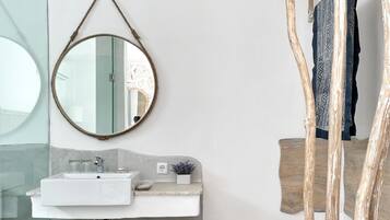 Un baño moderno con un espejo redondo, lavamanos blanco y banco de madera.